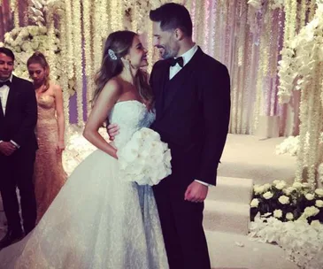 Bride and groom smiling at each other in a lavish wedding setting with white flowers and light-colored decor.