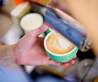 Barista pouring latte art into a green cup of coffee.