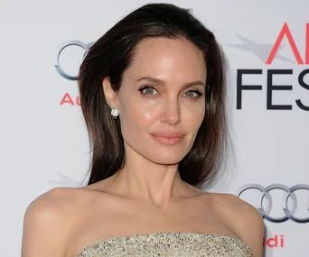 A woman with long hair in an elegant dress poses on the red carpet.