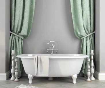 A classic white bathtub with clawfoot design, flanked by green curtains and tall candle holders.
