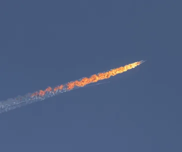 A jet engulfed in flames streaks across a clear blue sky after being downed.