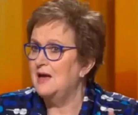 Amanda Vanstone speaking on TV, wearing glasses and a patterned blue outfit, with an expressive gesture.