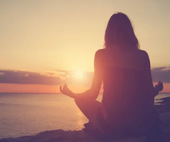 A person meditating by the ocean during a sunrise or sunset.