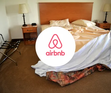 Hotel room with unmade bed, Airbnb logo overlay, suggesting improper use of rental property.
