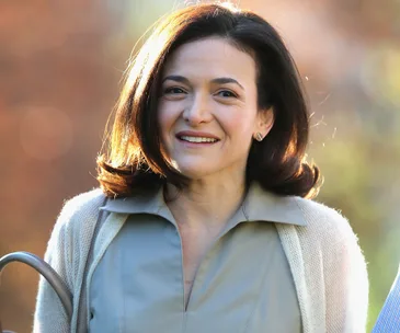 Sheryl Sandberg smiling outdoors, wearing a light-colored blouse and cardigan.
