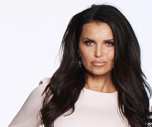 Suzi Taylor poses in a white textured dress with long dark hair styled loose, against a plain light background.