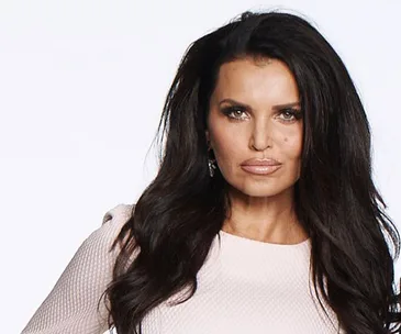 Suzi Taylor poses in a white textured dress with long dark hair styled loose, against a plain light background.