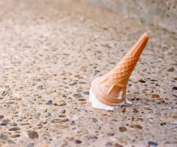 Ice cream cone dropped upside down on a textured concrete surface.