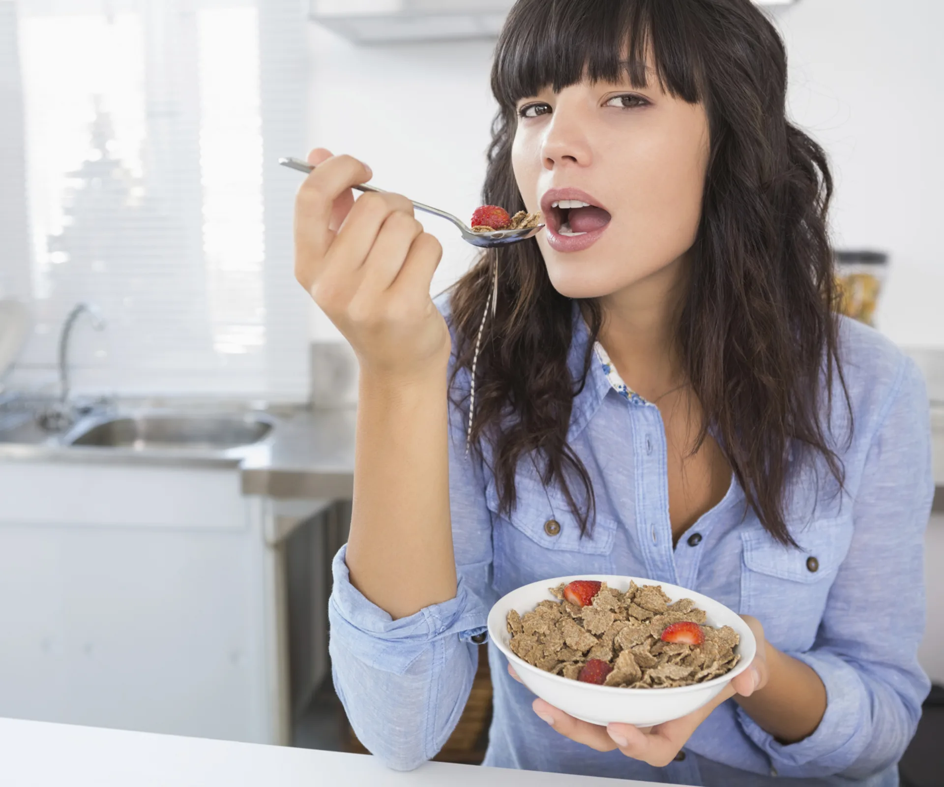 Woman eating cereal with strawberries in a modern kitchen.
