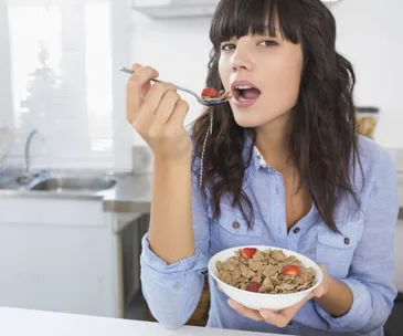 Woman eating cereal with strawberries in a modern kitchen.