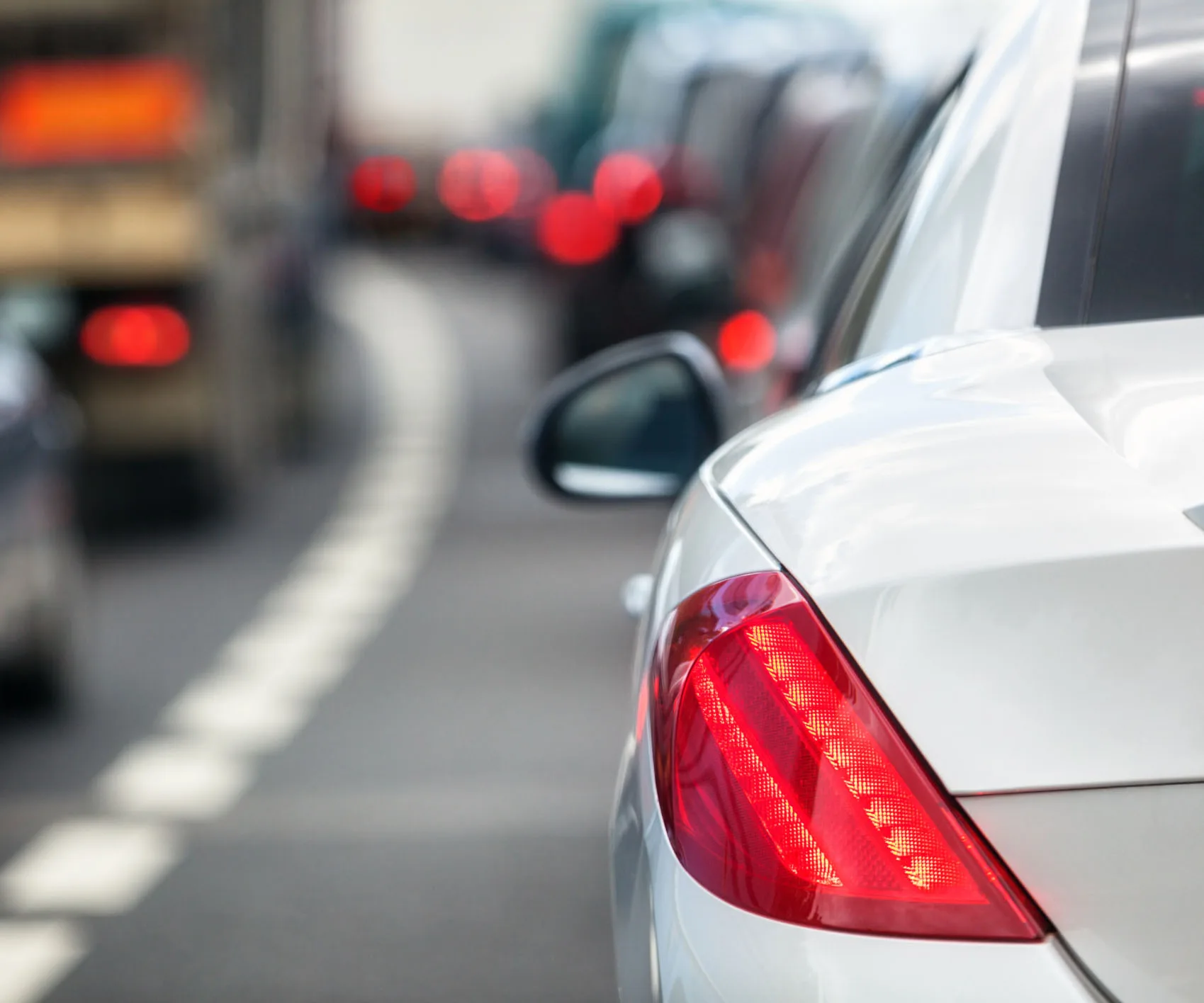 A silver car's rear brake light is illuminated in a traffic jam.