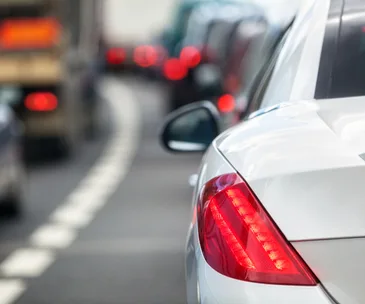 A silver car's rear brake light is illuminated in a traffic jam.