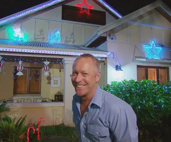House decorated with Christmas lights and ornaments, with a person smiling in front.