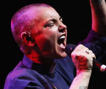 Singer passionately performing on stage, holding a microphone close to her mouth with eyes closed.
