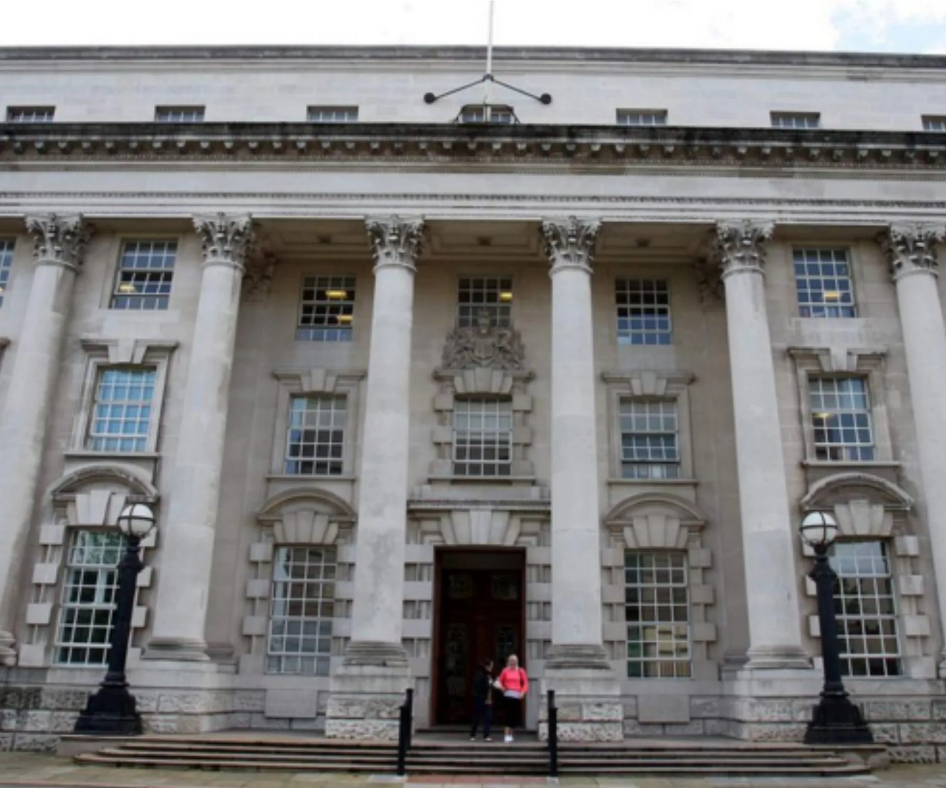 Front view of Belfast High Court building with columns and two people by the entrance.