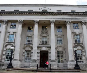 Front view of Belfast High Court building with columns and two people by the entrance.