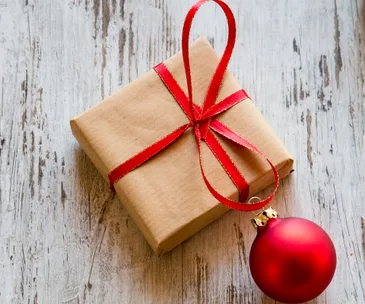 Brown gift with red ribbon and red ornament on rustic wooden surface.