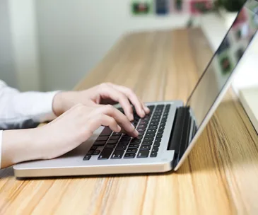 Hands typing on a laptop on a wooden desk.