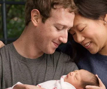 A couple lovingly gazes at their newborn wrapped in a patterned blanket, outdoors.
