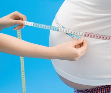 Person measuring a waist with a tape, highlighting obesity concerns against a blue background.