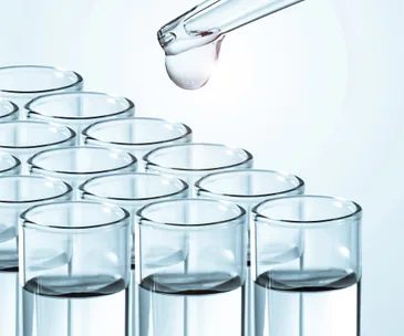 A pipette dropping liquid into glass test tubes, representing scientific research or laboratory testing.