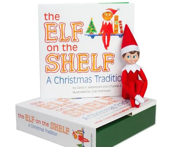 Elf on the Shelf figure sitting on a box, next to a book titled "The Elf on the Shelf: A Christmas Tradition."