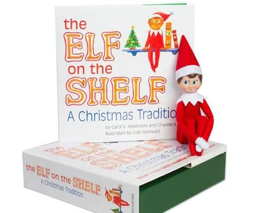 Elf on the Shelf figure sitting on a box, next to a book titled "The Elf on the Shelf: A Christmas Tradition."