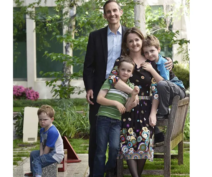 Family photo with four people posing happily and a child sitting apart, outdoors.