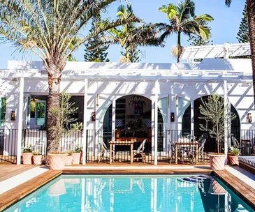 A luxurious poolside view at Halcyon House, featuring palm trees and a white terrace in bright sunlight.