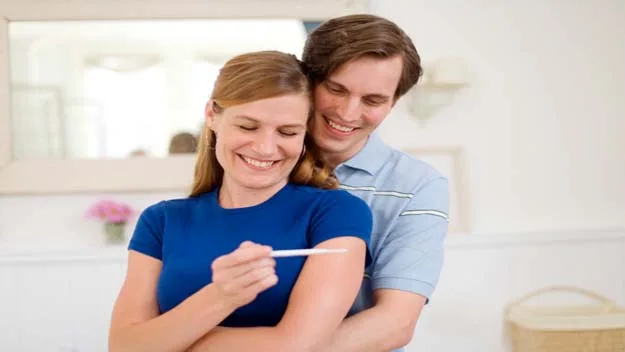 A smiling couple looks at a positive pregnancy test, symbolizing joy and anticipation in early pregnancy.