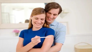 A smiling couple looks at a positive pregnancy test, symbolizing joy and anticipation in early pregnancy.
