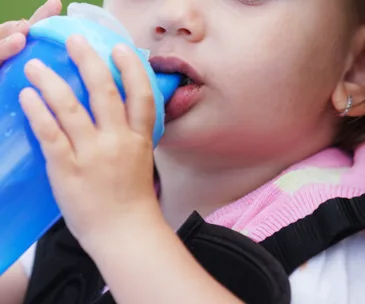 A toddler drinking from a blue sippy cup while wearing a pink bib.