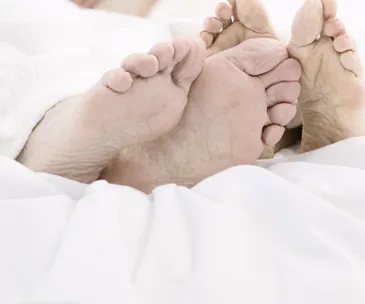 Two pairs of feet intertwined under white bedsheets.