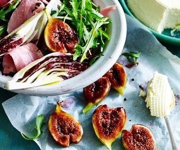 Salad with radicchio, arugula, ham, figs, and ricotta on a blue surface.