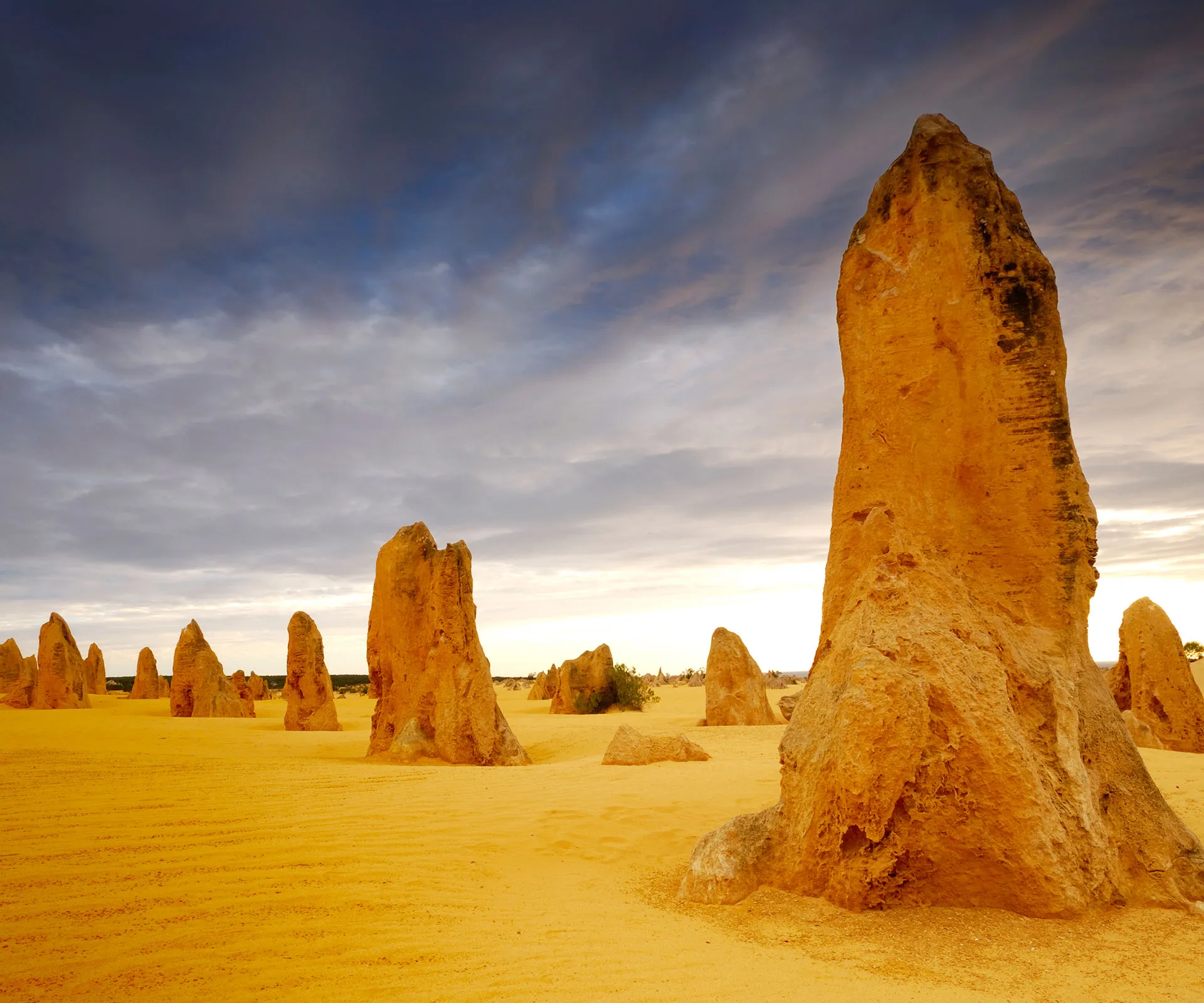 Yellow limestone formations rise from sandy terrain under a cloudy sky at the Pinnacles Desert in Nambung National Park, Australia.