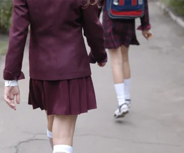 Two students in uniforms walking on a path, one with a backpack, from behind.