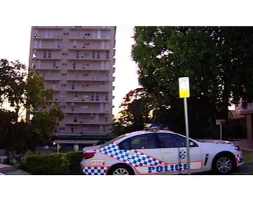 Police car parked in front of a multi-story building with trees nearby in an urban area.
