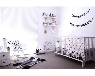 Minimalist monochrome nursery with a crib, wall art "Dream Big Little Fella," and modern furniture.