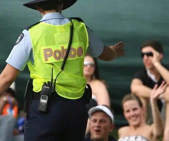Police officer in high-visibility vest interacting with seated people in a public setting.