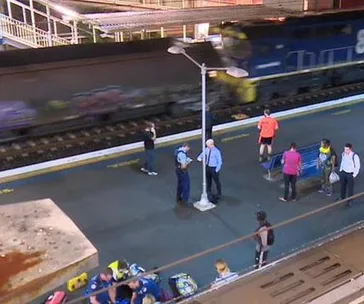 Police and bystanders on a train platform in Sydney with a moving train and scattered belongings on the ground.