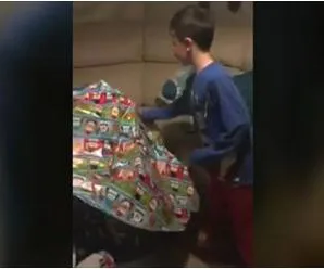 Boy in blue shirt unwraps large, colorful present with excitement, hinting at a heartfelt surprise inside.