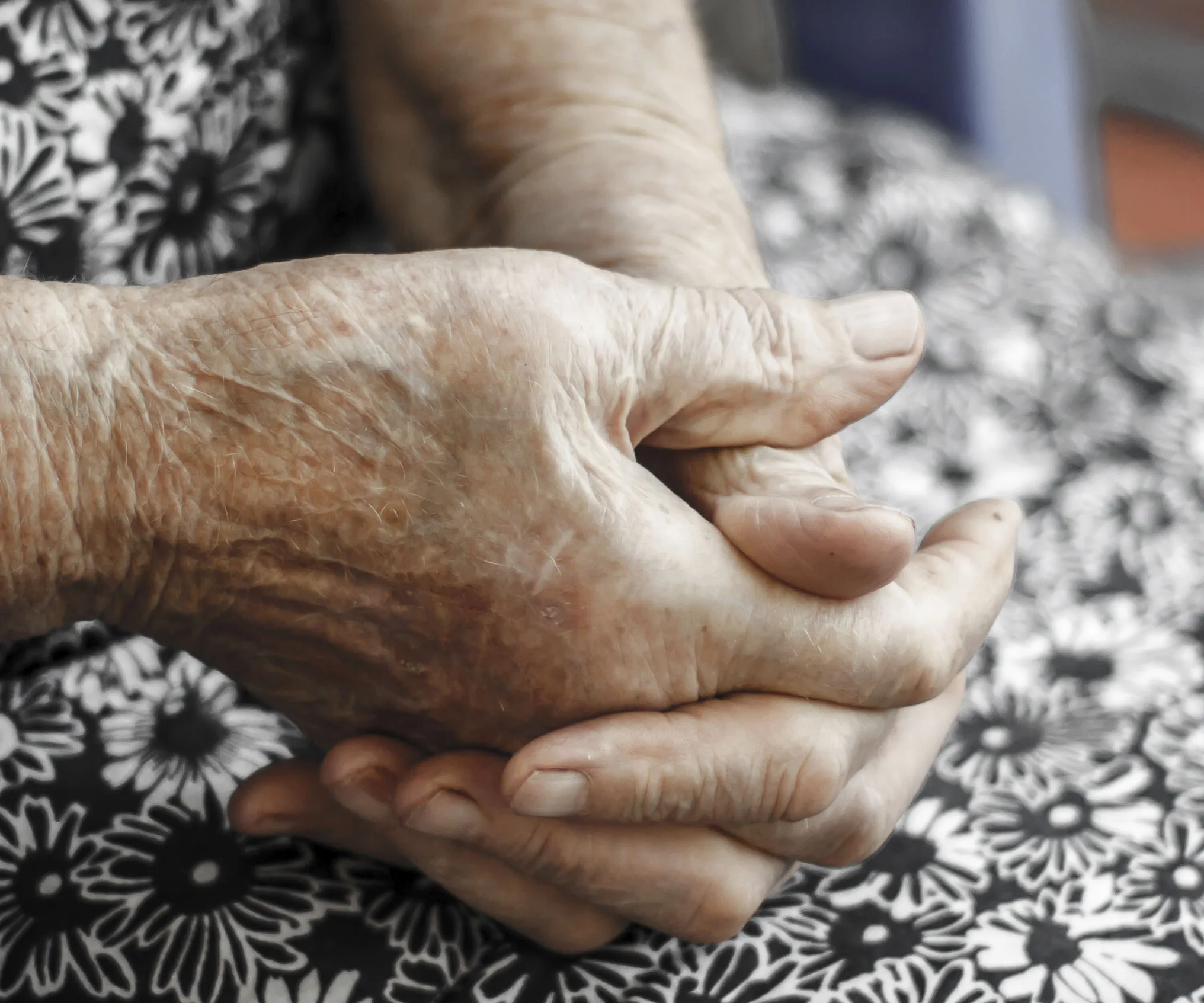Elderly person's hands clasped together on floral fabric background.