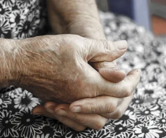 Elderly person's hands clasped together on floral fabric background.