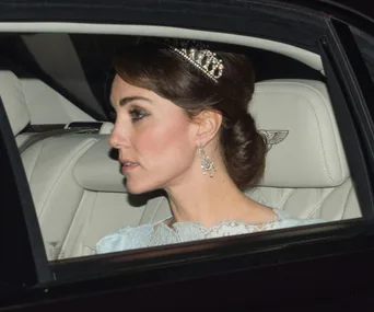 Royalty in a car wearing a jeweled tiara and earrings, gazing forward.