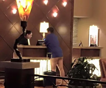 A person in a blue shirt appears to be pantsless at a hotel reception desk.