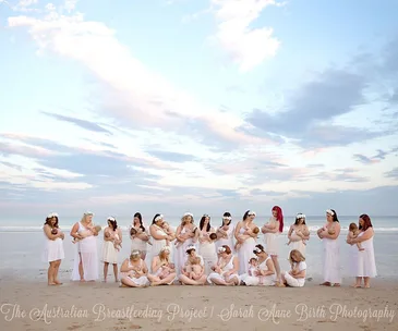 Women in white dresses breastfeeding their babies on a beach, promoting the Australian Breastfeeding Project.
