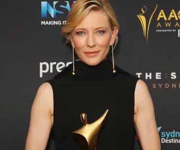 Woman in black dress holding AACTA Award trophy, posing against branded backdrop at awards ceremony.