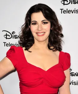 A woman with dark hair smiles in a red dress at a Disney Television event backdrop.