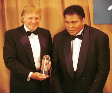 Two men in tuxedos, one holding an award, standing together at an event.