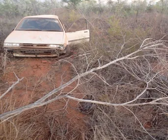 Abandoned car in a dry, overgrown field with open door and a missing wheel.